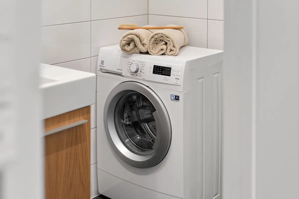A washing machine with rolled towels on top in a white utility room.