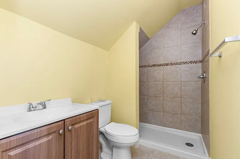 A small shower room with a toilet and wood vanity